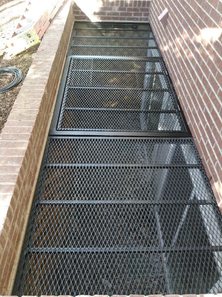 Black mesh grate over a window well next to brick