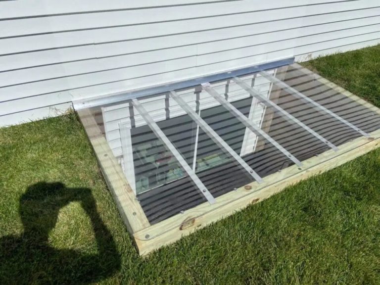 Clear window well cover with support bars beside a lawn