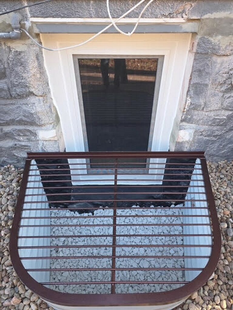 Egress window behind a dark grate in a stone foundation