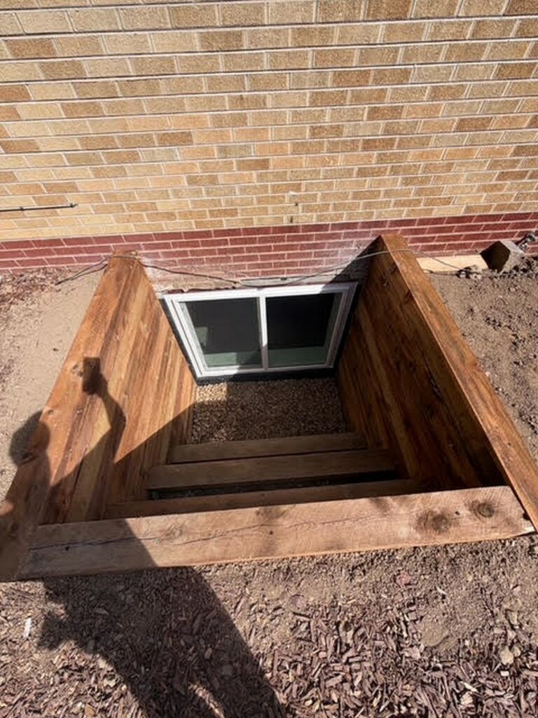 Timber window well with steps outside a brick home