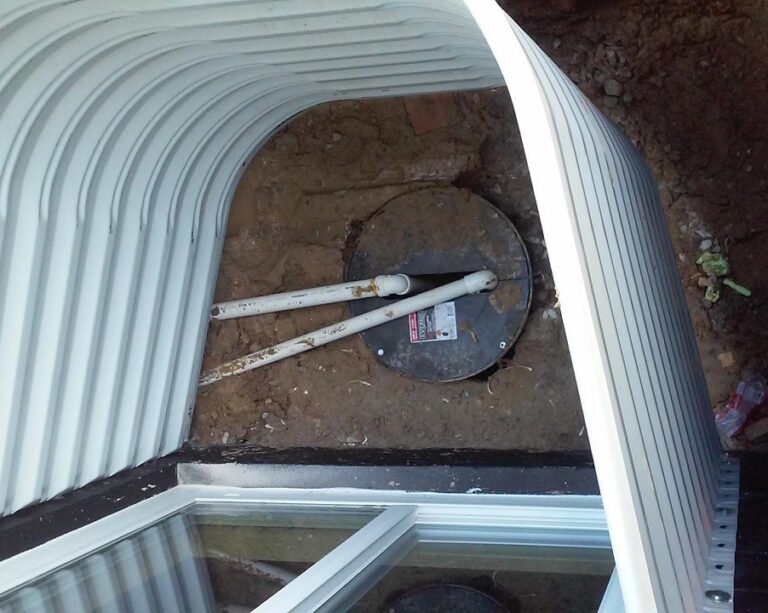 Sump pump and discharge pipe at the bottom of a steel window well