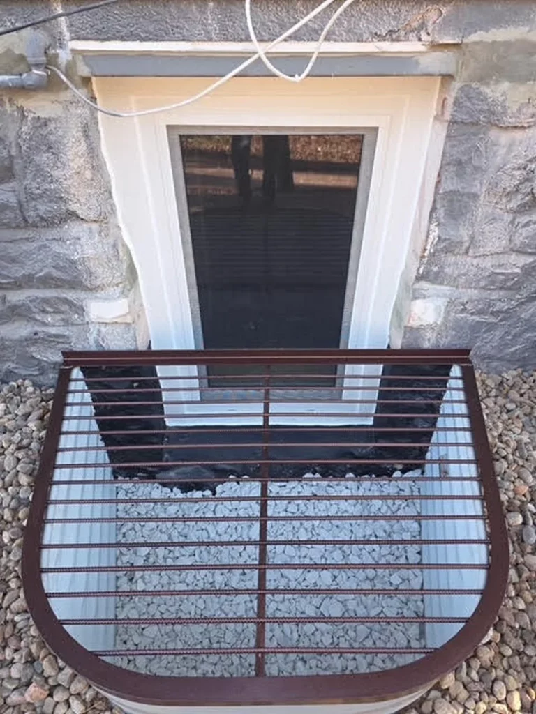 Tilt-and-turn egress window in a stone foundation with a Boman Kemp well and bar grate